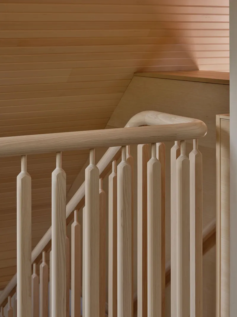 Close-up of the timber staircase balustrade with turned spindles and curved handrail against horizontal wood walls