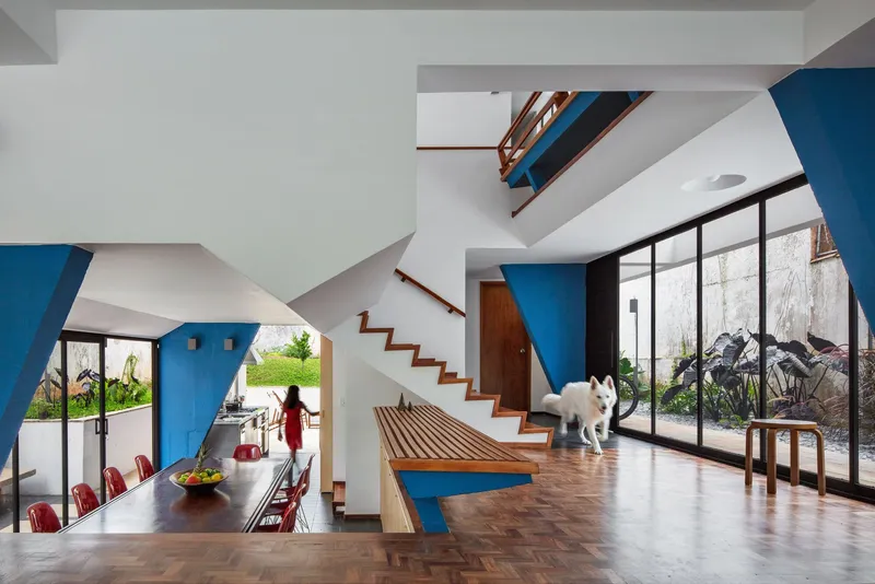 Double-height living space with timber staircase, angled blue columns, and dog on herringbone floor