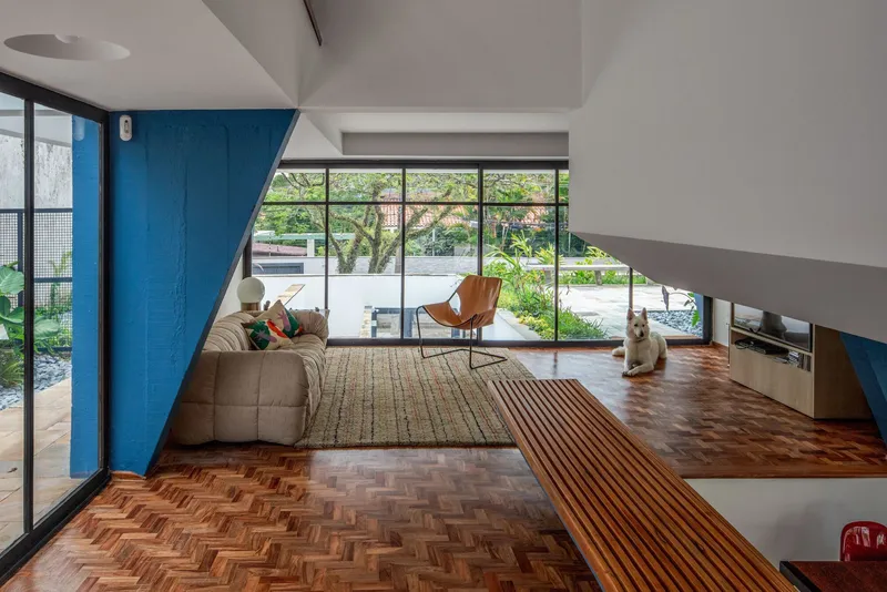 Split-level interior with herringbone parquet flooring and angled blue structural elements beside glazed courtyard