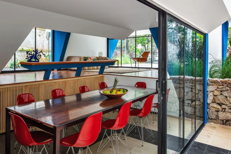 Dining area with red chairs overlooking raised living level separated by angled blue beam