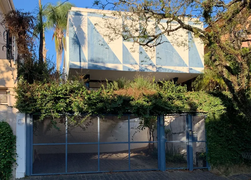 View from street showing cantilevered volume with geometric facade behind mesh gate and bare tree