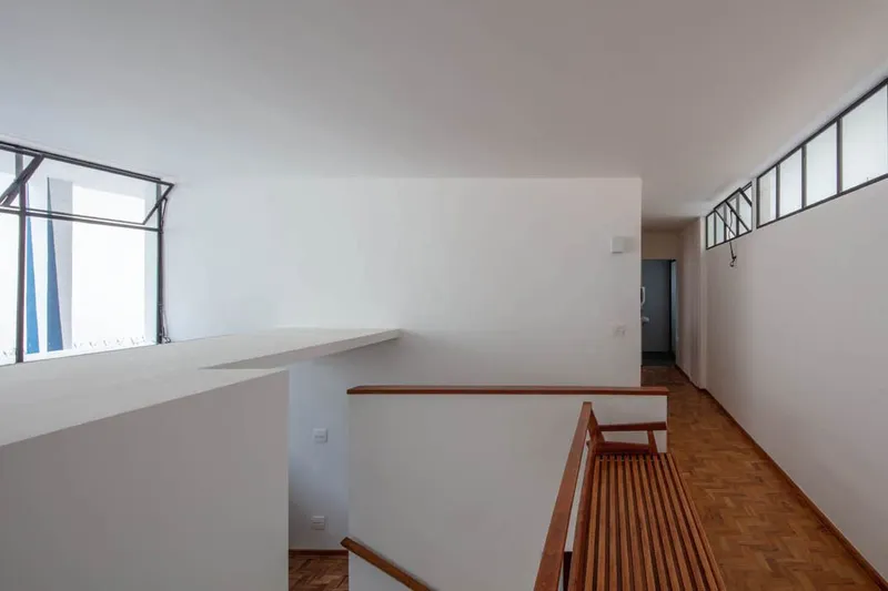 Upper level hallway with wooden railing overlooking stairwell and white walls lit by clerestory windows