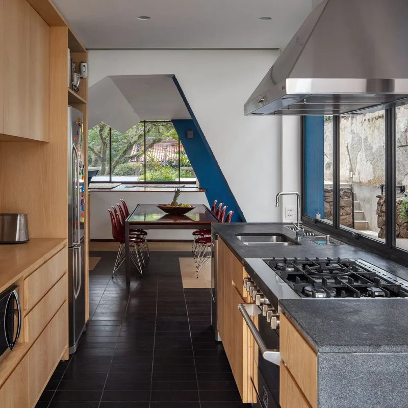Kitchen with light wood cabinetry and dark floor tiles looking through to dining area and garden