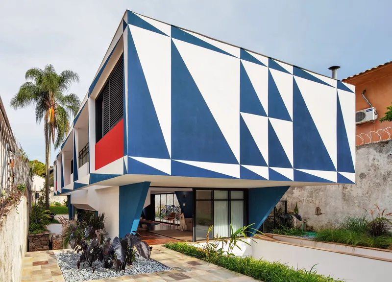 Cantilevered upper volume with blue and white triangular painted facade above courtyard with palm trees