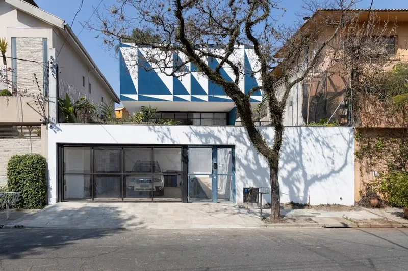 Street facade with glazed garage door and white boundary wall casting bare tree shadows