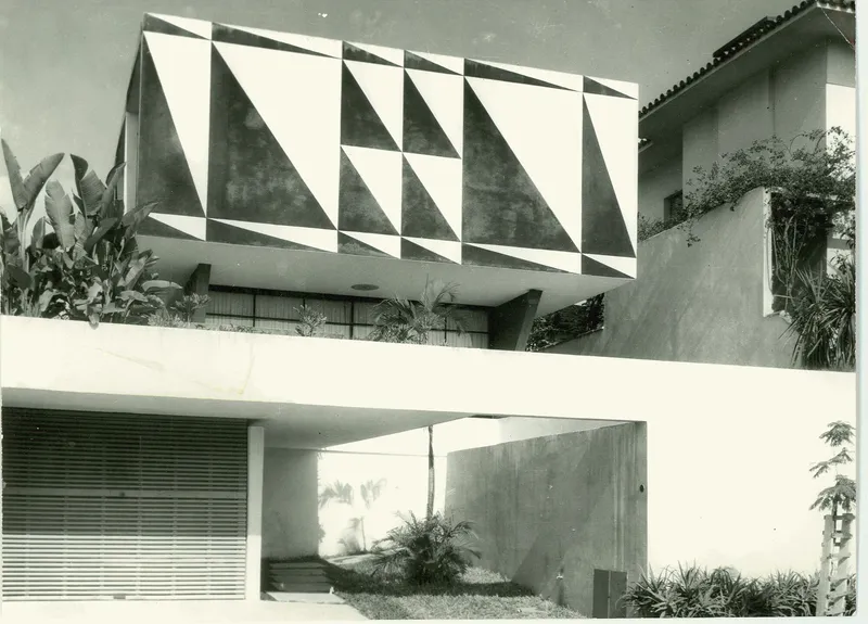 Upper volume with geometric triangular facade panels above a recessed entry courtyard with planted beds