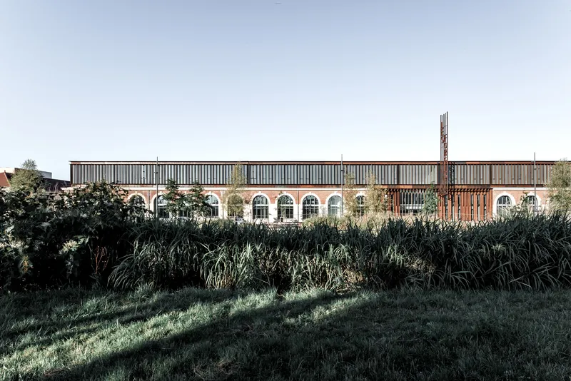 Long view of the brick facade with arched openings seen across wild grasses in early morning light