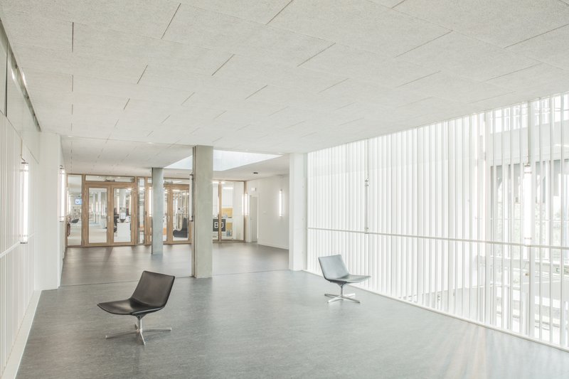 Interior lobby with vertical white screen walls, polished concrete floor and two lounge chairs