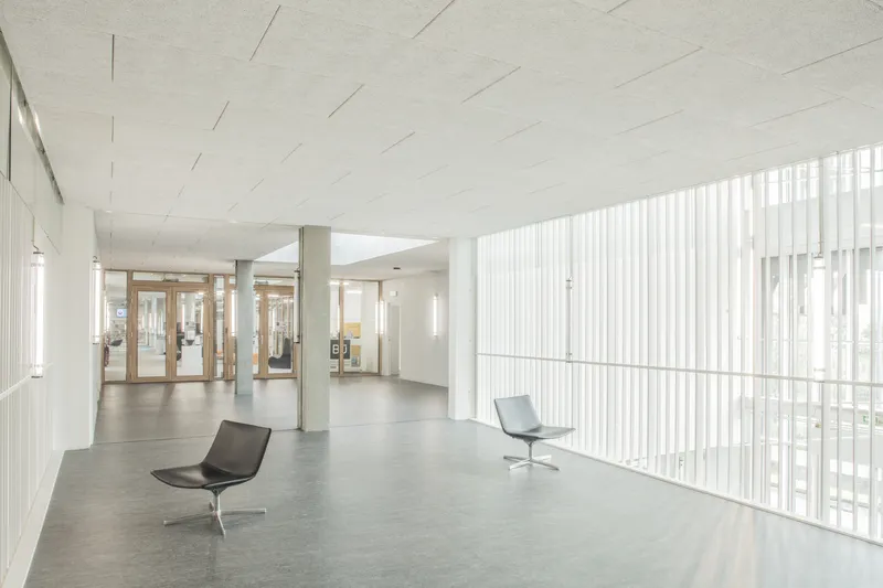 Interior lobby with vertical white screen walls, polished concrete floor and two lounge chairs