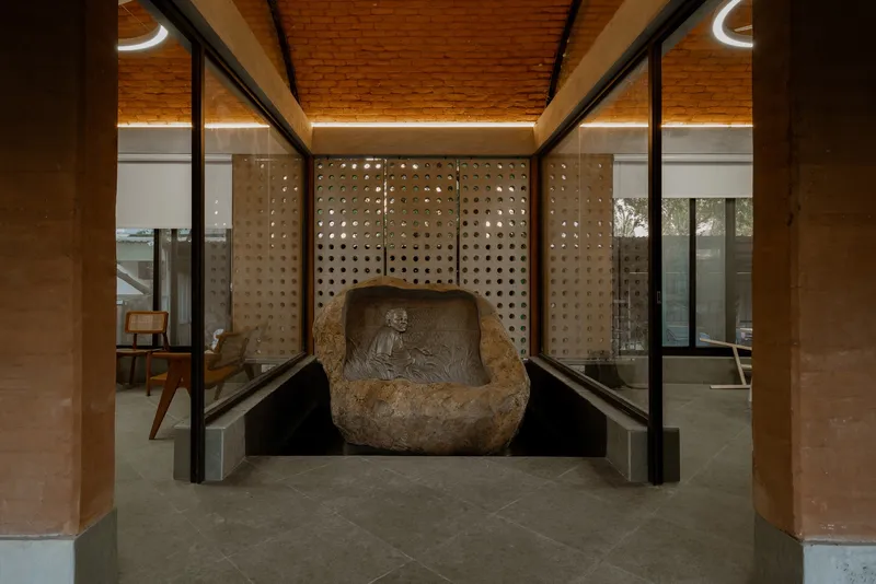 Carved stone sculpture set within a perforated wall niche flanked by glass partitions at dusk