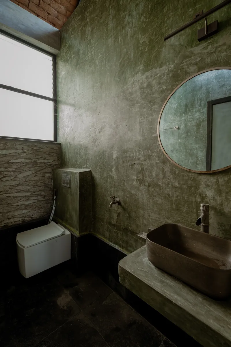 Bathroom with textured plaster walls, round mirror, stone vessel sink, and high corner window