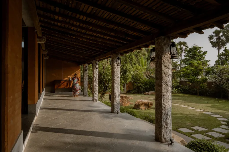 Covered veranda with exposed timber ceiling and cylindrical stone columns overlooking a garden lawn