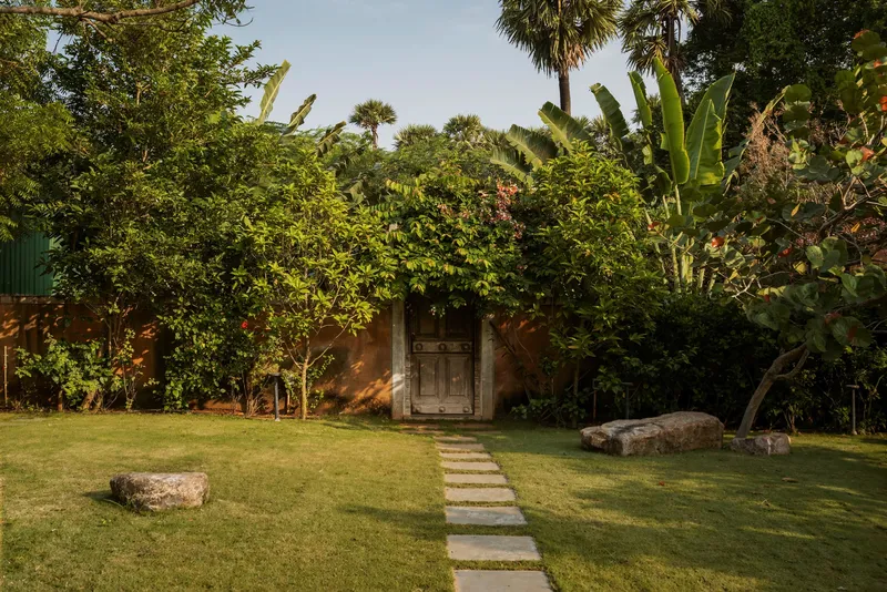 Stone pathway through lawn leading to a wooden door set within a planted earth wall