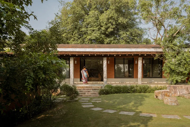 Single-story pavilion with stone columns and terracotta tile roof set in a garden with stepping stone path