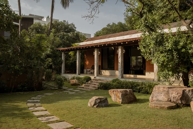Open veranda with rough stone columns and ochre walls facing a lawn with large rock formations