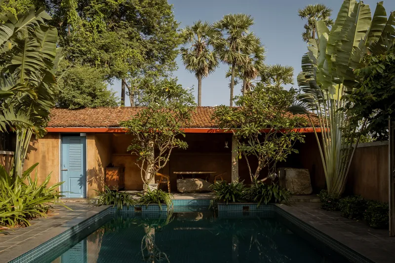 Rear courtyard with reflecting pool, terracotta roof, and tropical planting including palms and banana trees