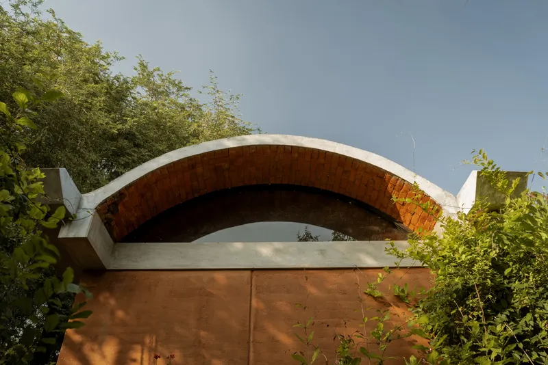 Exterior view of the exposed brick vault with concrete edge beam framed by foliage