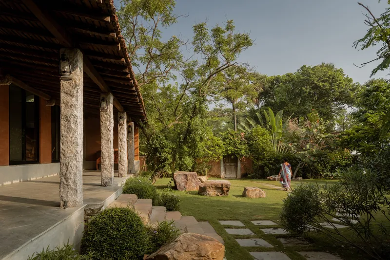 Covered veranda with stone columns and timber roof overlooking a garden with stepping stones and a visitor walking