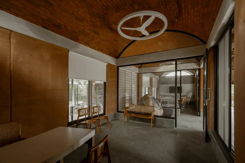 Interior living space with woven timber ceiling vault and glass doors opening to a courtyard with sculpture