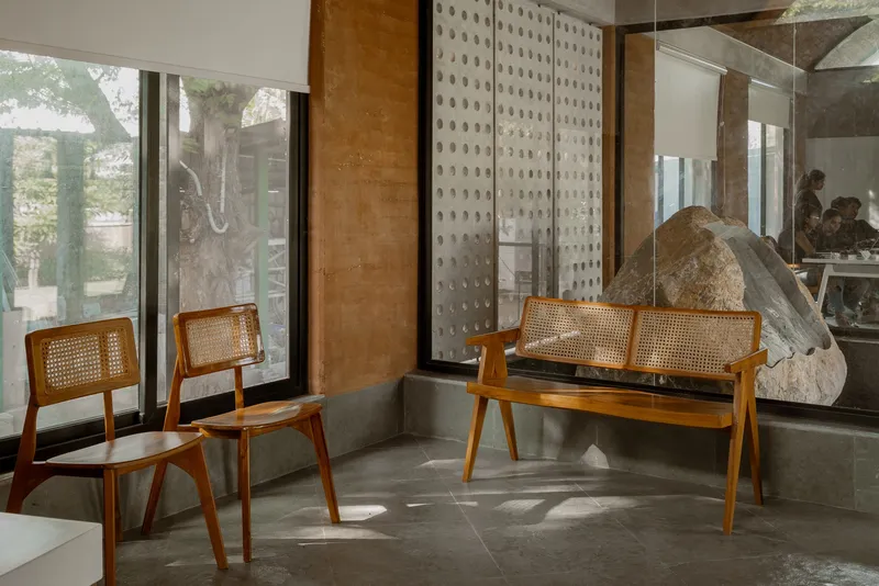Seating nook with caned timber chairs and bench beside perforated stone screen wall in afternoon light