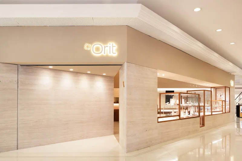 Storefront entrance clad in pale travertine with illuminated signage and polished white floor tiles