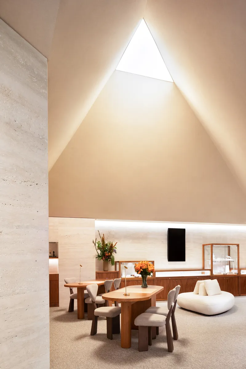 Interior seating area under a vaulted ceiling with backlit triangular skylight and timber furniture