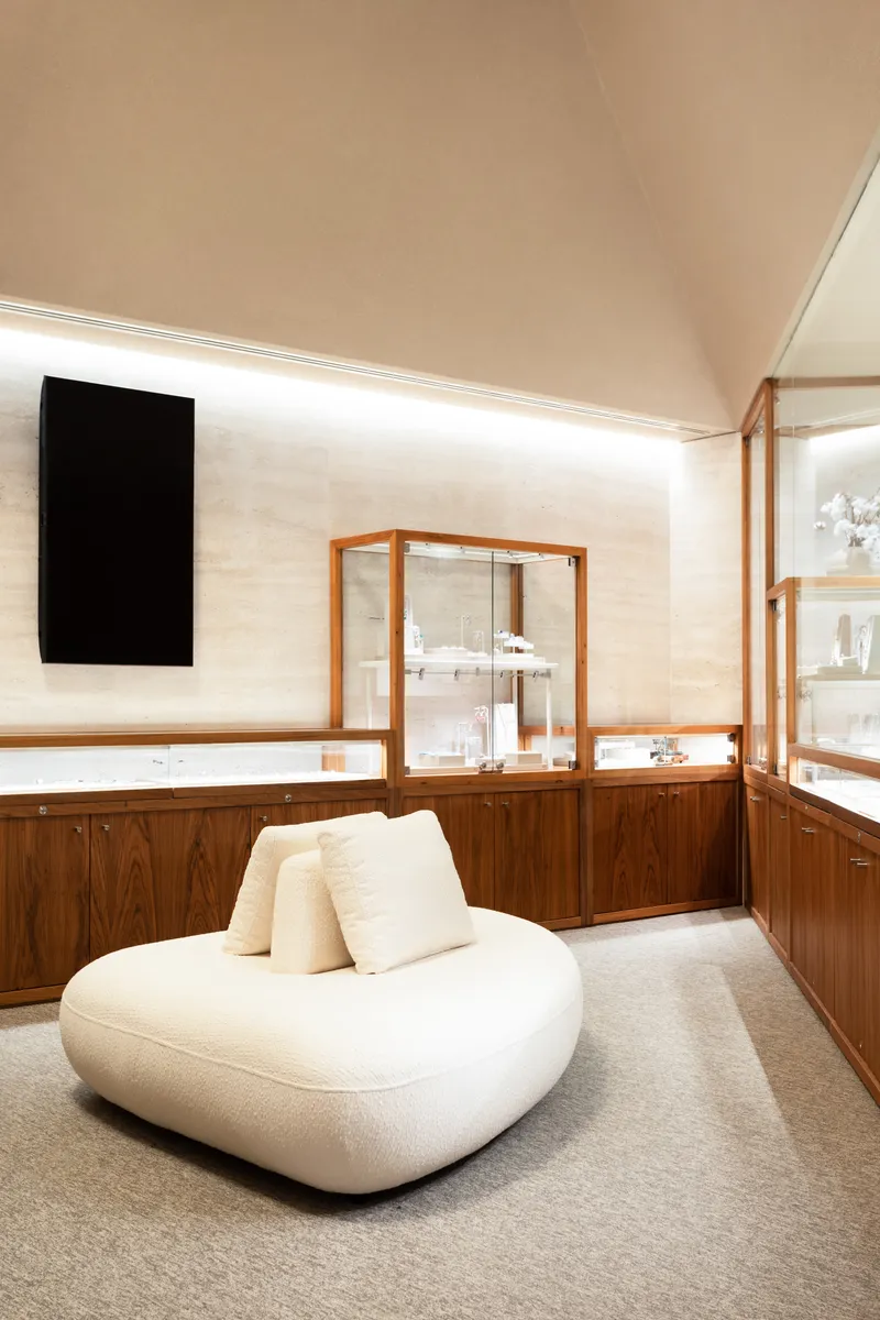 Curved seating beneath angled ceiling with walnut millwork and framed glass vitrines along the wall
