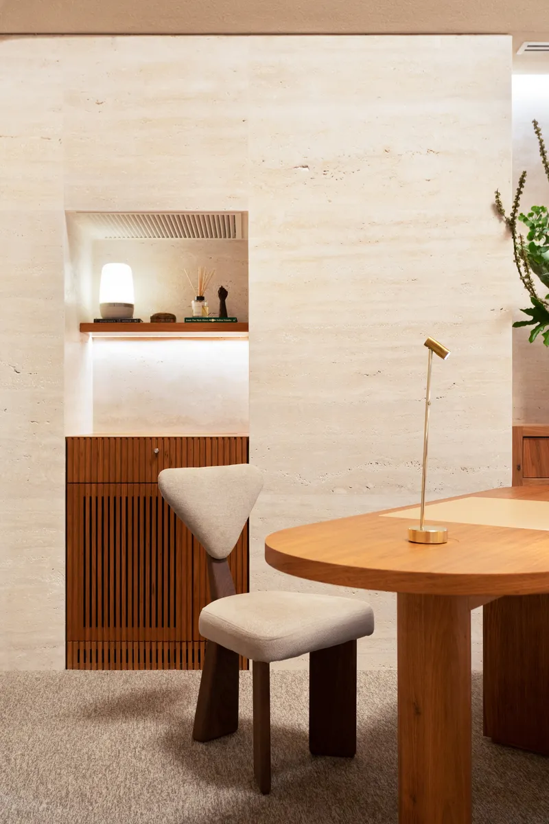 Timber work surface with triangular upholstered stool beside a rammed earth wall and wall niche