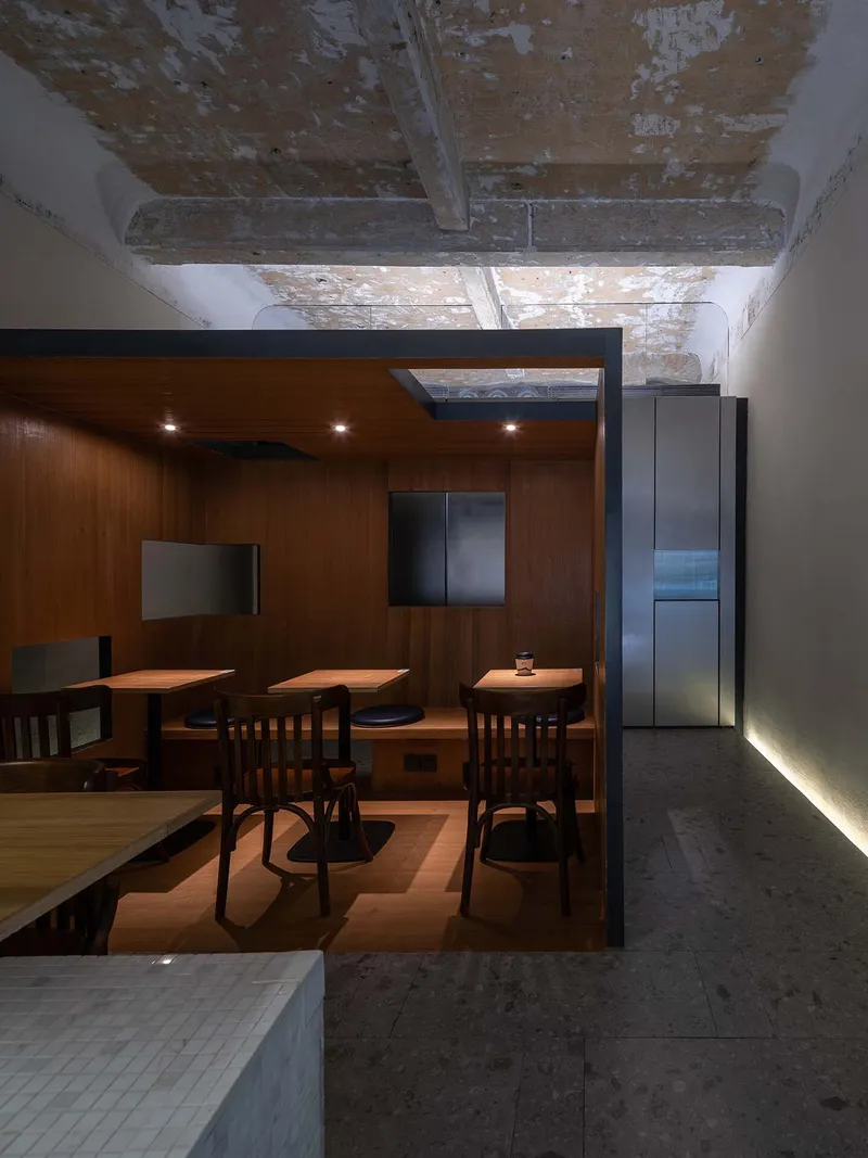 Wood-paneled dining enclosure with embedded tables beneath distressed concrete beam ceiling