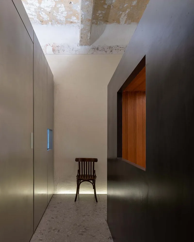 Narrow corridor with a single chair between metal wall panels and an exposed concrete ceiling