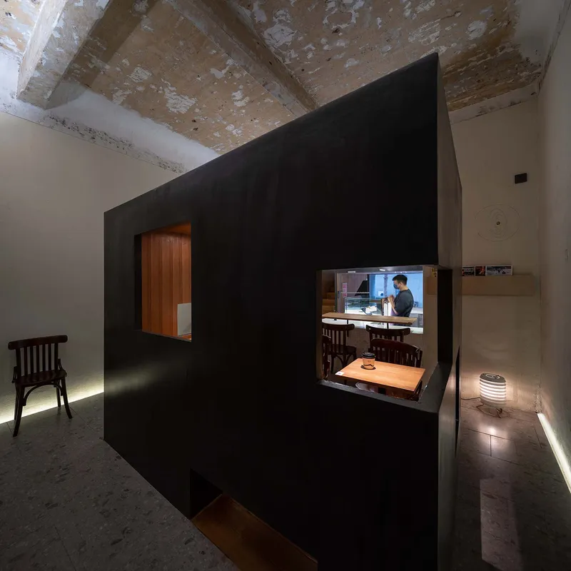 Dark steel volume inserted within a whitewashed space beneath an exposed timber ceiling with peeling paint