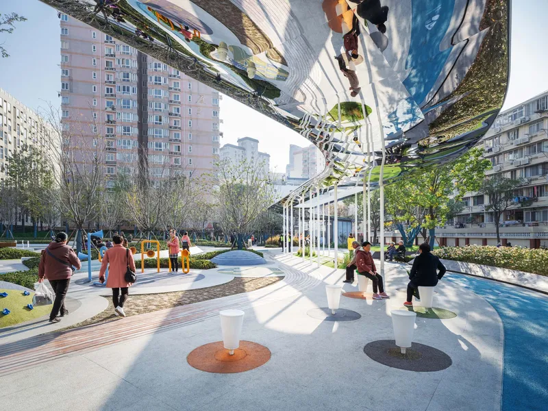 Courtyard plaza with reflective overhead canopy and circular ground insets where residents gather in afternoon light
