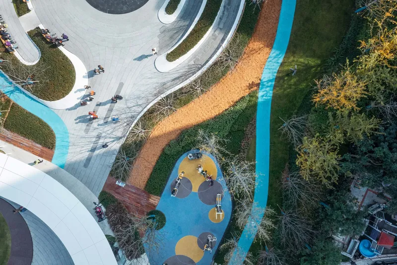 Aerial view of the circular playground with blue rubberized surfacing among curved planted beds and pathways