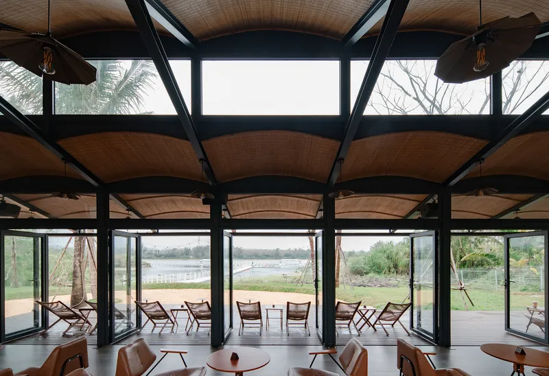 Interior view showing arched woven ceiling panels suspended between black steel trusses with clerestory windows above
