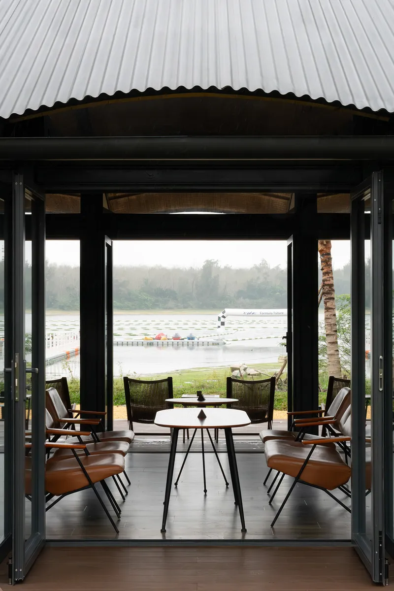 Framed view through the pavilion opening toward the misty lake with dining furniture in the foreground