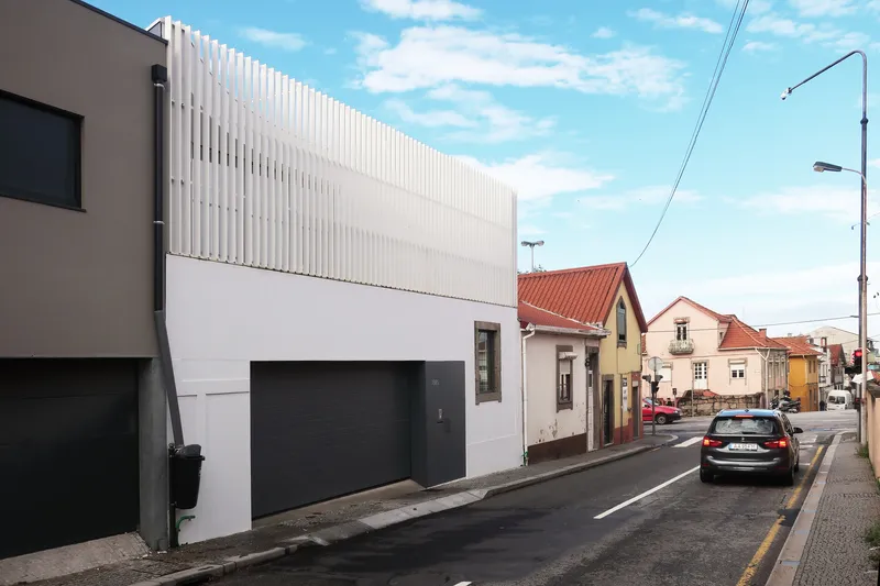 Street view of the white plastered facade with vertical metal louvers above the garage opening