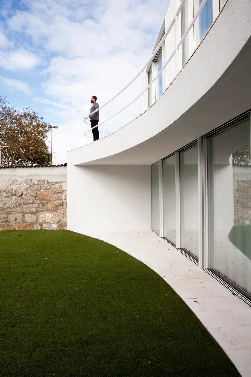 Curved terrace balcony with sliding glass doors overlooking a lawn and stone boundary wall