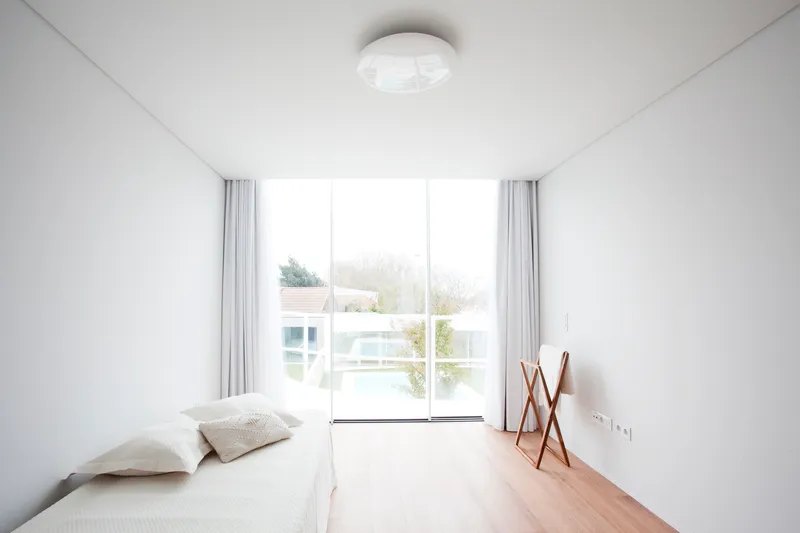 Bedroom with light wood flooring and glazed doors opening to a planted terrace beyond