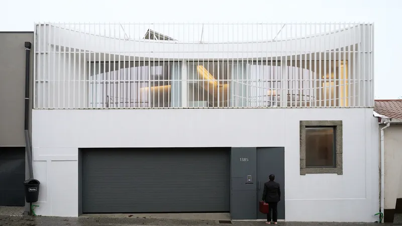 Street elevation at dusk showing the illuminated curved balcony screen and a figure at the entrance