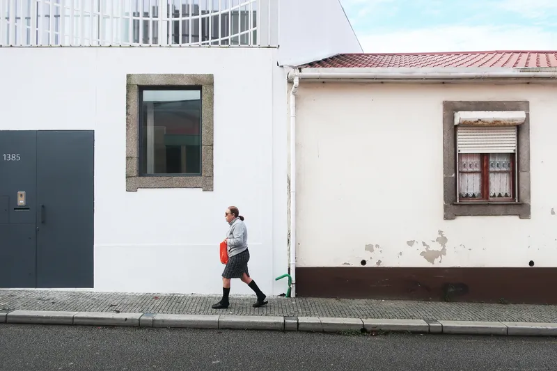Street view of white rendered facade with granite-framed window and grey door, person walking past