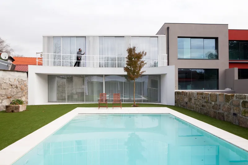 Garden facade with pool, vertical aluminum louvers and stacked volumes with a figure on the upper balcony