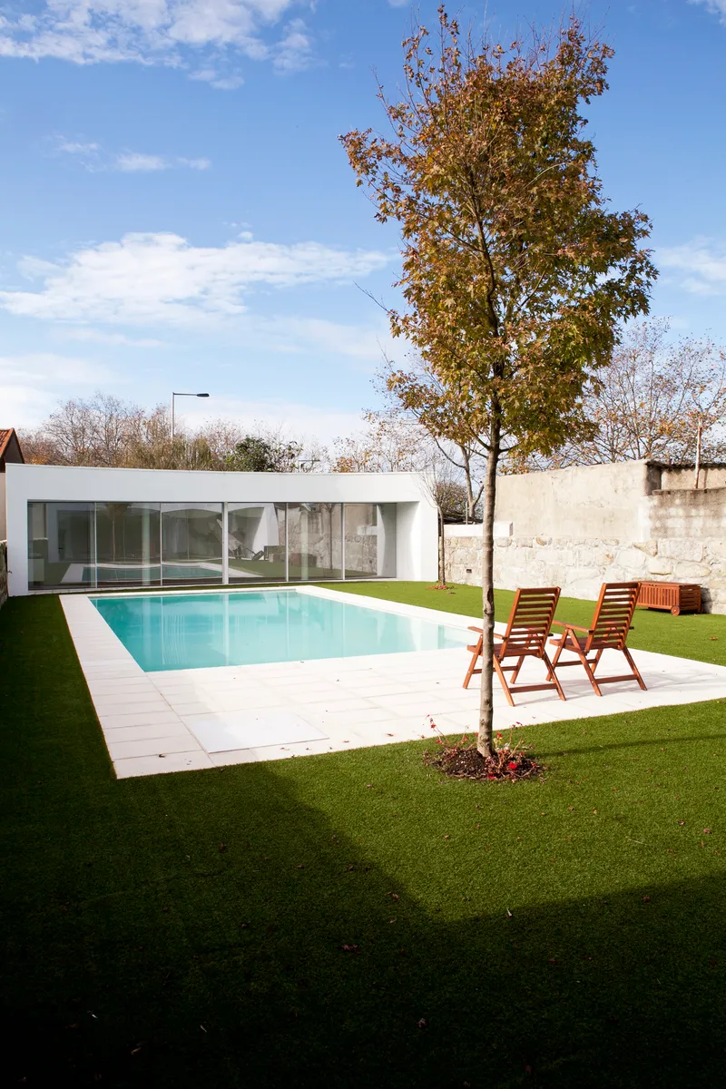 Rear lawn with planted tree, poolside deck and low white pavilion under autumn sky