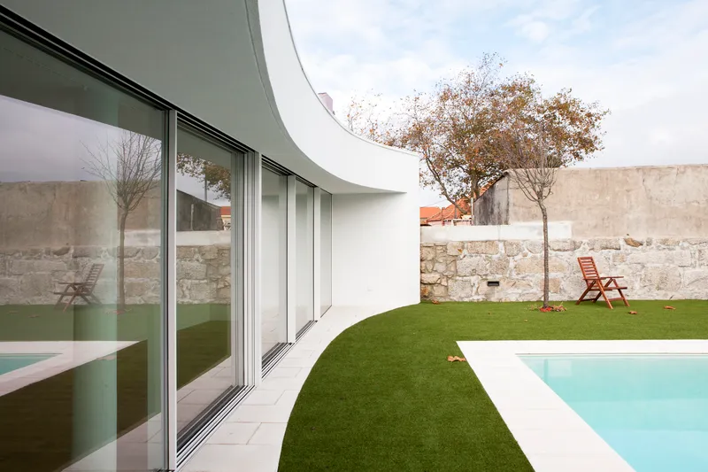 Private courtyard with curved white wall, sliding glass doors, artificial lawn, and pool beside stone wall