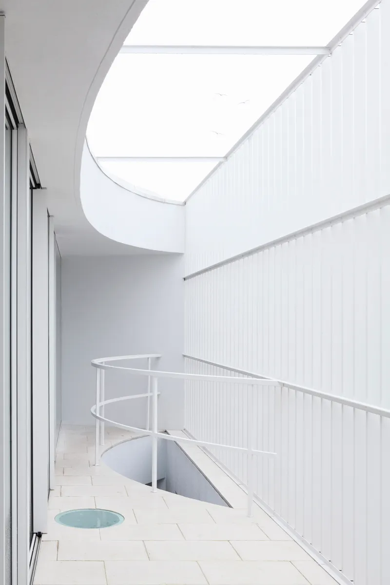 Upper terrace with curved roof overhang, tiled floor, metal balustrade, and skylight opening