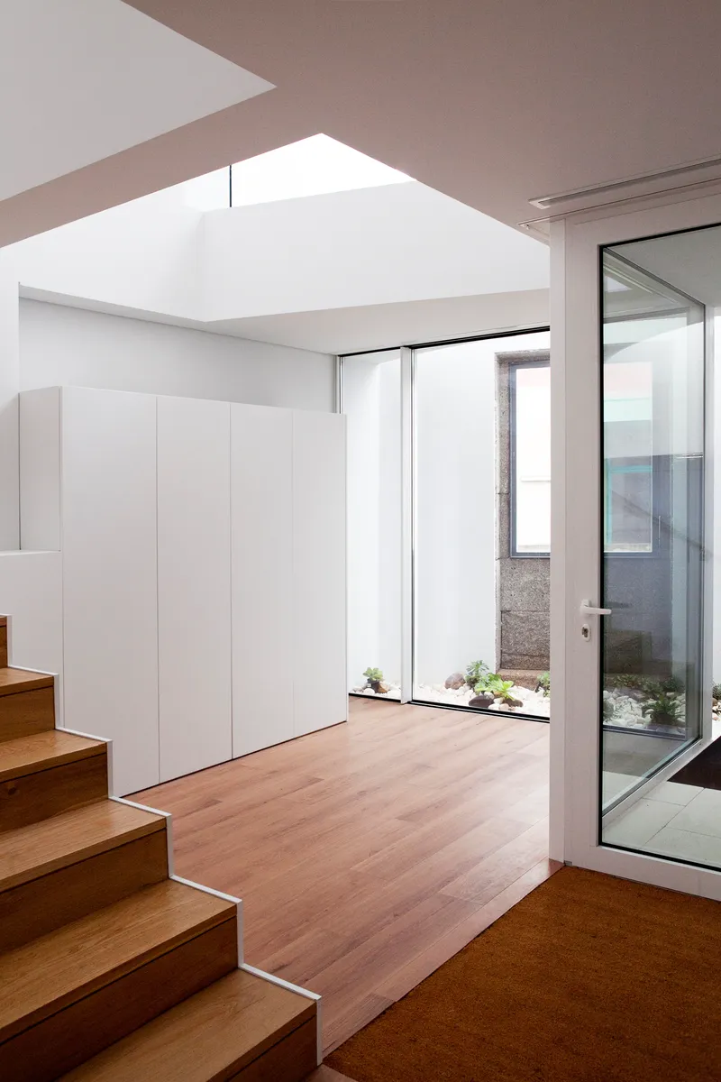 Interior view of timber staircase beside white storage wall with skylight overhead and courtyard window