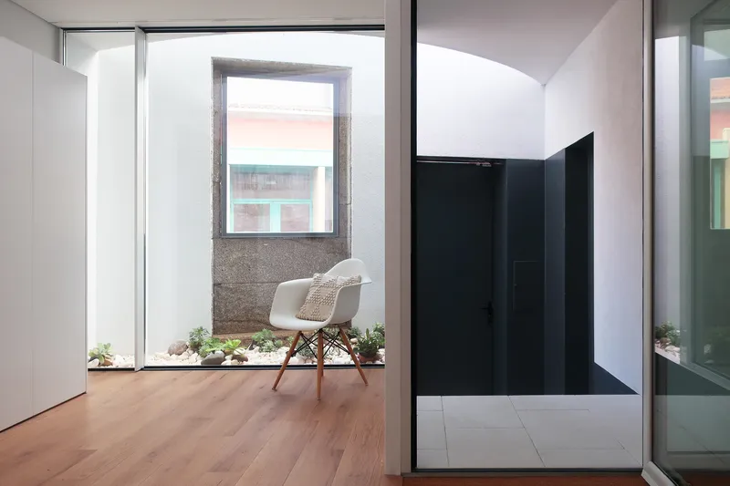 Interior courtyard with granite-framed window, planted bed at base, and white chair on timber floor