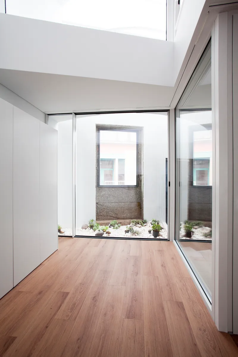 Corridor with timber flooring leading to internal courtyard with planted bed and granite walls