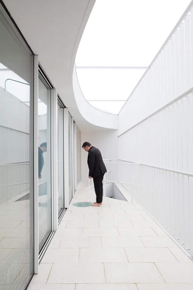 Outdoor terrace with white tile flooring and a person beside a curved skylight opening
