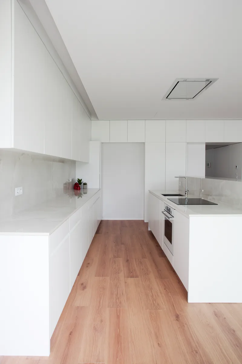 White kitchen with handleless cabinetry, recessed ceiling vent and pale timber flooring