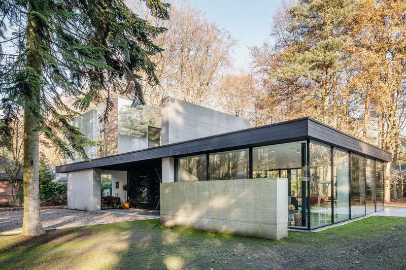 Flat-roofed pavilion with blackened timber overhang and concrete walls amid autumn trees
